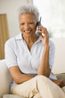 © Monkey Business - Woman sitting in living room using telephone and smiling