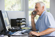 Man in home office on telephone using computer