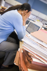 Businesswoman in cubicle with stacks of files