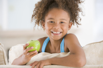 Young girl eating apple in living room smiling