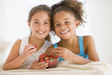 Two Young Girls Eating Strawberries In Living Room Smiling