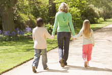 Mother And Two Young Children Walking On Path Holding Hands Smil