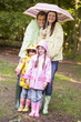 © Monkey Business - Family outdoors in rain with umbrella smiling