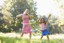 Woman And Young Girl Outdoors Using Hula Hoops And Smiling