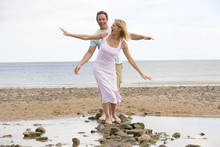 Couple At The Beach Walking On Stones And Smiling