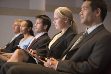 Wall Mural - Five businesspeople sitting in presentation room with clipboards