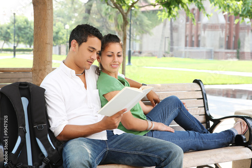 Fotografie, Obraz Attractive students at college sitting on bench reading