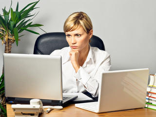 Young beautiful business lady at a table with two laptops.