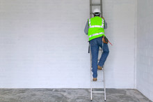 Workman In Reflective Vest And Hard Hat Climbing A Ladder