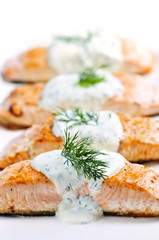 Cooked salmon fillets with dill sauce on white plate