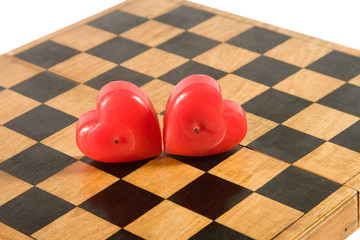 Two heart-shaped red candles on an old chessboard