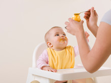 Studio Shot Of Mother Feeding Hungry Baby In Highchair