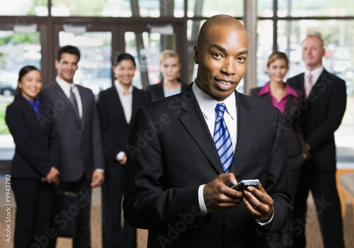 African businessman using cell phone in front of co-workers Plakát