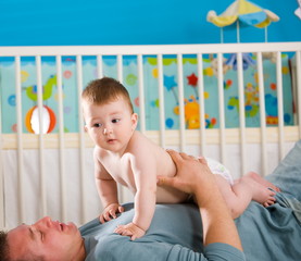 Father lying on back and lifting baby boy ( 1 year old ) at home