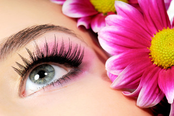 close-up of woman green eye. pink flower on background.