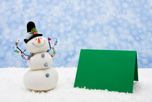 Snowman With A Green Blank Card On Snowflake Background
