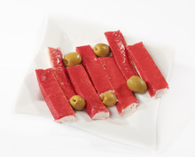 Surimi Sticks In A Plate With Olives On A White Background