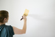 Woman painting white wall with bright yellow paint