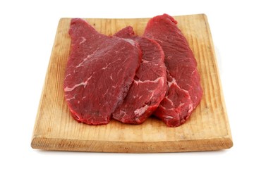 Three raw steaks on a wooden chopping board