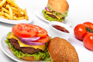 cheeseburgers, one's top mooved and french fries and tomatoes