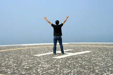 young man with arms open contemplating the ocean