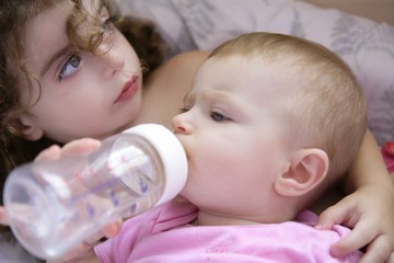 Toddler girl giving bottle of milk to baby sister