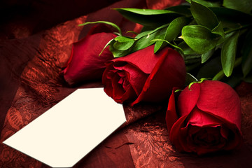 Three red roses against a red background with a white card.