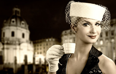 Canvas Print - Beautiful young woman drinking coffee. Old city background behin