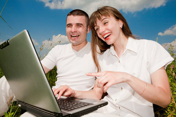 Wall Mural - Casual happy couple on a laptop computer outdoors