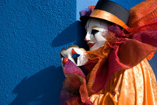 Clown Holding Mask In Front Of Blue Wall
