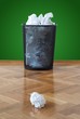 Wastepaper bin full of crumpled paper balls one on floor