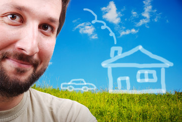 Young male smiling on green meadow with abstract house