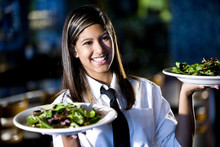 Hispanic Waitress Serving Two Plates Of Salad In A Restaurant