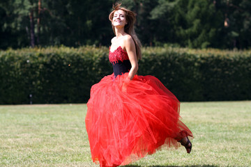 Beautiful joyful woman in a red dress running on meadow in park