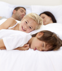 Wall Mural - Little girl smiling on bed wile her family sleep