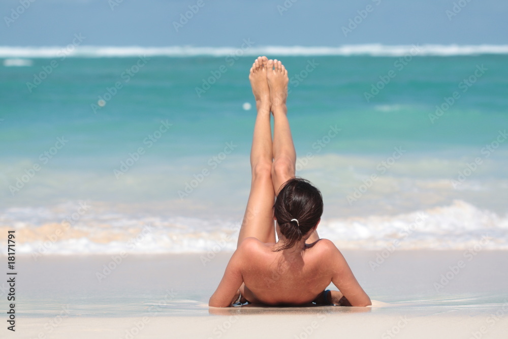 Kobieta leżąca na plaży na plecach z uniesionymi nogami - obrazy, fototapety, plakaty 