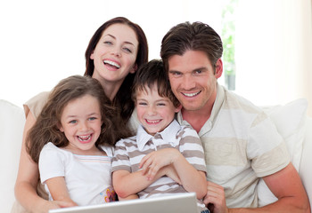 Wall Mural - Smiling family using a laptop in the living-room