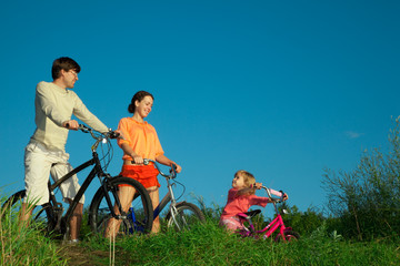 Wall Mural - Family from three persons on bicycles. Parents look at a daughte