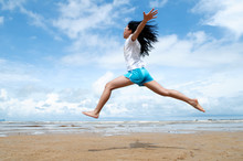 Young Girl Leaping In The Air With Her Hands Raised On The Beach