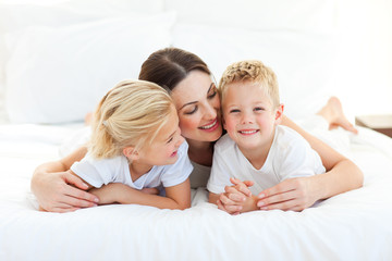 Wall Mural - Cute children and their mom having fun lying on a bed