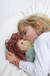 canvas print picture - Kleines Maedchen liegt mit Puppe schlafend im Bett.