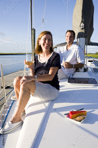 Fotografie, Obraz Mid-adult couple sitting on deck of boat enjoying drink