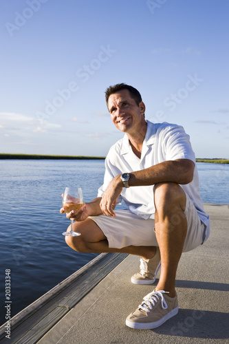 Fotografie, Obraz Mid-adult man on dock by water enjoying drink on sunny day