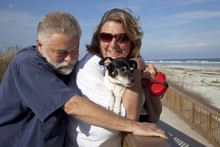 Older Middle-aged Couple With Their Dog At The Beach