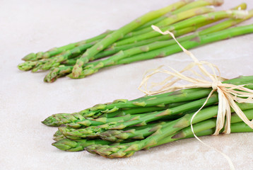 Two bunches of fresh asparagus on tile counter top.