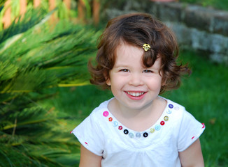 Portrait of a little cute smiling girl in a green summer garden