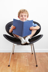 Young boy sitting in a chair reading a book