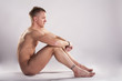 Naked young male sits in front of a grey background