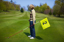 Woman Holding Yellow Flag With Number Two On The Golf Course.
