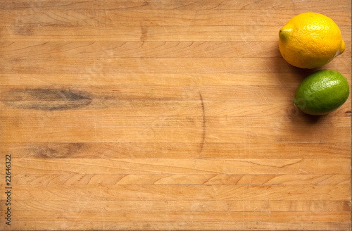 Fotografie, Obraz Lemon and lime on a worn butcher block cutting board